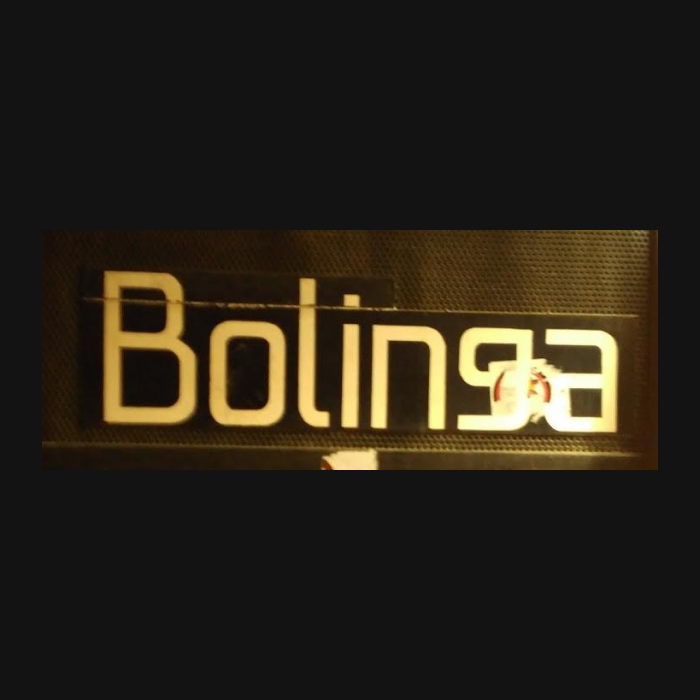 La imagen muestra el nombre "Bolinga" en letras mayúsculas y de color claro, probablemente blanco o beige, destacándose sobre un fondo oscuro que parece ser una rejilla o malla metálica. El texto tiene una tipografía moderna y limpia, con líneas rectas y anchas. En la parte derecha de la imagen, justo al final de la palabra, hay un diseño o ilustración que no se distingue completamente, pero que parece contener un toque de color, posiblemente rojo o anaranjado. El letrero tiene un aspecto contemporáneo y podría estar iluminado desde atrás, lo que daría un efecto luminoso alrededor de las letras y acentuaría su visibilidad contra el fondo texturizado. Este tipo de señalización es común en bares, restaurantes o locales nocturnos que buscan un diseño moderno y llamativo.