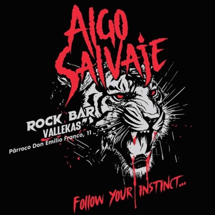 La imagen presenta un diseño gráfico dramático para promocionar "Algo Salvaje", un bar de rock en Vallekas. Destaca un tigre de bengala con una expresión feroz y agresiva en colores blanco, negro y rojo. Sus ojos rojos brillan intensamente, y la boca abierta revela colmillos afilados, con detalles que sugieren movimiento y ferocidad. El título "Algo Salvaje" está en letras grandes y estilizadas de color rojo en la parte superior, contrastando fuertemente con el fondo negro. Debajo del tigre, en letras más pequeñas pero igualmente impactantes, se encuentra la dirección del bar y el lema "Follow your instinct..." (Sigue tu instinto...), invitando al espectador a experimentar la intensidad y la pasión del lugar.